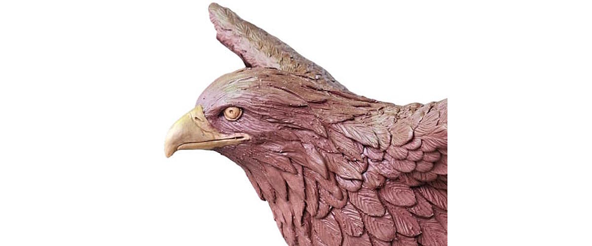 Close-up of a detailed clay sculpture of a peregrine falcon's head, showing realistic feather textures, hooked beak, and lifelike eye before mold making and bronze casting.